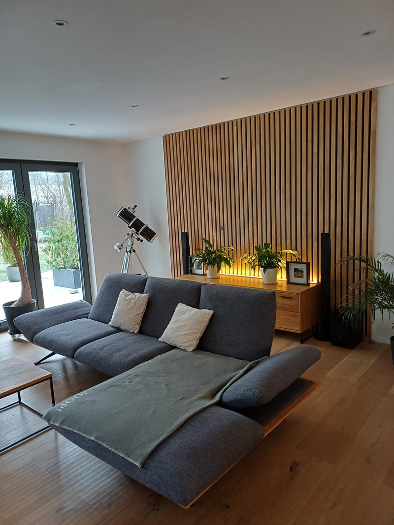 Wohnzimmer mit Akustikpaneelen aus Eiche, am Wandfuß hinter dem Sideboard leuchtet indirektes LED-Licht